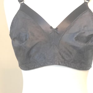 May include: A black bra with adjustable straps and a small bow detail at the center. The bra has a classic design with a smooth, matte finish. The bra is displayed on a white mannequin.