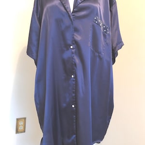 May include: A navy blue satin sleep shirt with a collared neckline and short sleeves. The collar and pocket feature a white polka dot pattern. The shirt has a button-down front and a single pocket.