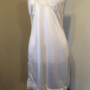 May include: A white satin slip dress with delicate lace trim on the neckline and hem. The slip has adjustable straps and a flattering shape. The dress is displayed on a mannequin.