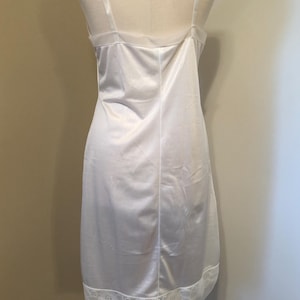 May include: A white satin slip dress with spaghetti straps and a lace trim at the hem. The dress is displayed on a mannequin. This classic lingerie piece has a simple, elegant design. The dress is a classic lingerie piece.