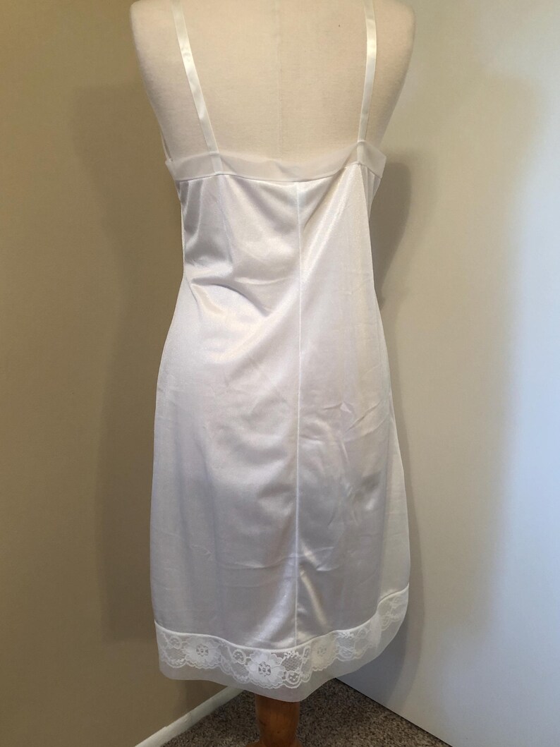 May include: A white satin slip dress with spaghetti straps and a lace trim at the hem. The dress is displayed on a mannequin. This classic lingerie piece has a simple, elegant design. The dress is a classic lingerie piece.