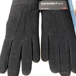 Op de afbeelding: Een paar zwarte handschoenen met een Thinsulate Flex Insulation-label. De handschoenen zijn gemaakt van een zacht materiaal en hebben gestikte details op de achterkant van de hand en vingers. Het label geeft 40 gram isolatie aan.