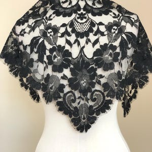May include: A triangular black lace shawl featuring an intricate floral pattern with scalloped edges. The delicate fabric displays a detailed botanical design with interconnected leaves and blossoms, creating a semi-sheer texture throughout the piece.