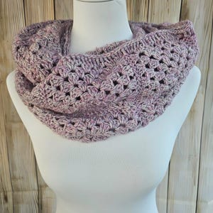 Könnte beinhalten: Handgehäkelter Cowl-Schal in Lavendel-, Rosa- und Weißtönen. Der Schal wird auf einer weißen Schaufensterpuppe präsentiert und weist ein offenes, durchbrochenes Muster auf. Der Cowl ist zum Tragen um den Hals konzipiert und ist ein gemütliches Accessoire.