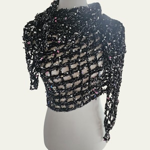 May include: A black, open-weave shawl with white and iridescent accents. The shawl is draped over a mannequin, showcasing its textured, net-like design. The accents include small, colorful sequins.