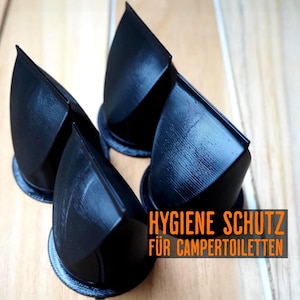 May include: Four black, geometric, cone-shaped objects with rounded bases are arranged on a light wood surface. The objects are angled towards the viewer. Text in orange reads "HYGIENE SCHUTZ FÜR CAMPERTOILETTEN."