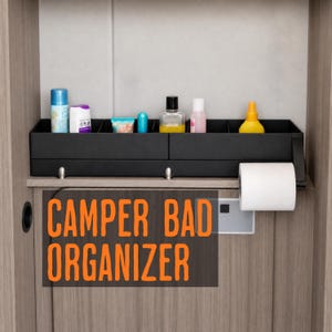 Op de afbeelding: Een zwarte rechthoekige badkamerorganizer met meerdere vakken voor diverse toiletartikelen en een rol wit toiletpapier op een zijhouder. De tekst CAMPER BAD ORGANIZER is in het oranje op het onderste gedeelte gedrukt.
