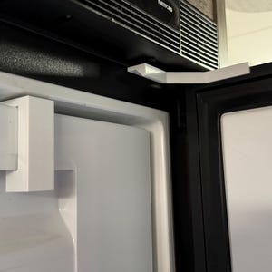 Può includere: Primo piano di una porta del frigorifero bianca con un chiavistello bianco. La porta è chiusa e il chiavistello è in posizione di blocco.
