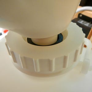 Könnte beinhalten: Nahaufnahme eines weißen Kunststoffbehälters mit passendem Deckel. Der Deckel hat eine Reihe vertikaler Rippen um seinen Umfang. Ein kleiner weißer Wasserhahn ist an der Seite befestigt. Der Behälter dient wahrscheinlich zur Aufbewahrung von Flüssigkeiten.