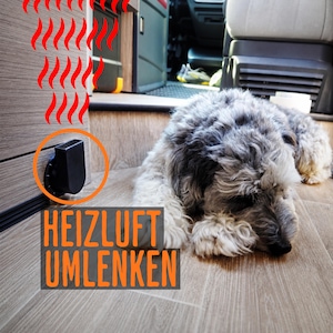 May include: A black plastic air vent deflector mounted on a wood-grain wall panel, featuring red graphic heat wave lines above it and the orange text HEIZLUFT UMLENKEN below, with a grey and white dog lying on the floor nearby.