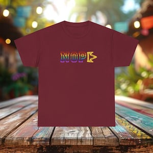 May include: A maroon t-shirt with the word "NOPE" in rainbow-colored letters. The "P" has a yellow arrow pointing to the right. The shirt is made of a soft material and is suitable for casual wear.
