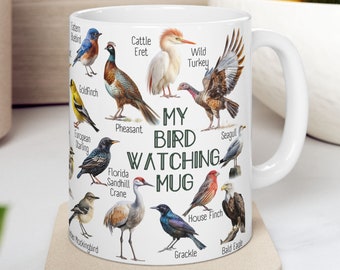 May include: White ceramic mug featuring illustrations of various bird species, including a bluebird, goldfinch, and bald eagle. The mug has the text "MY BIRD WATCHING MUG" printed on it. The mug is sitting on a beige coaster.