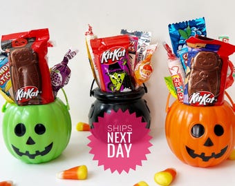 Könnte beinhalten: Drei Halloween-Süßigkeitenkörbe. Ein grüner Kürbis-Eimer, ein schwarzer Kessel und ein orangefarbener Kürbis-Eimer sind mit verschiedenen Süßigkeiten gefüllt, darunter Kit Kat-Riegel. Gezuckerter Mais ist um die Körbe verstreut.