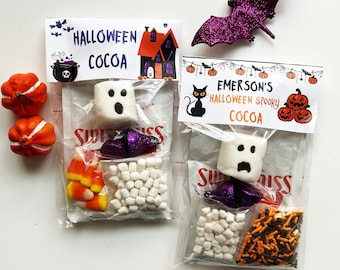 May include: Two clear plastic bags filled with Halloween-themed hot cocoa mix ingredients. The bags have labels that say "Halloween Cocoa" and "Emerson's Halloween Spooky Cocoa". The bags contain marshmallows, candy corn, sprinkles, and chocolate pieces.