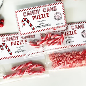 Puede incluir: Rompecabezas de bastones de caramelo en bolsas transparentes, con diferentes niveles de dificultad: Principiante, Intermedio y Experto. Cada rompecabezas está etiquetado con "Candy Cane Puzzle". También se ven bastones de caramelo rojos y blancos.