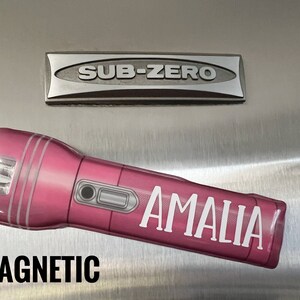 Peut inclure: Une lampe de poche magn&eacute;tique rose avec le nom "AMALIA" en lettres blanches. Le mot "MAGNETIC" est imprim&eacute; en lettres noires en gras sous la lampe de poche. Un embl&egrave;me argent&eacute; "SUB-ZERO" est au-dessus.