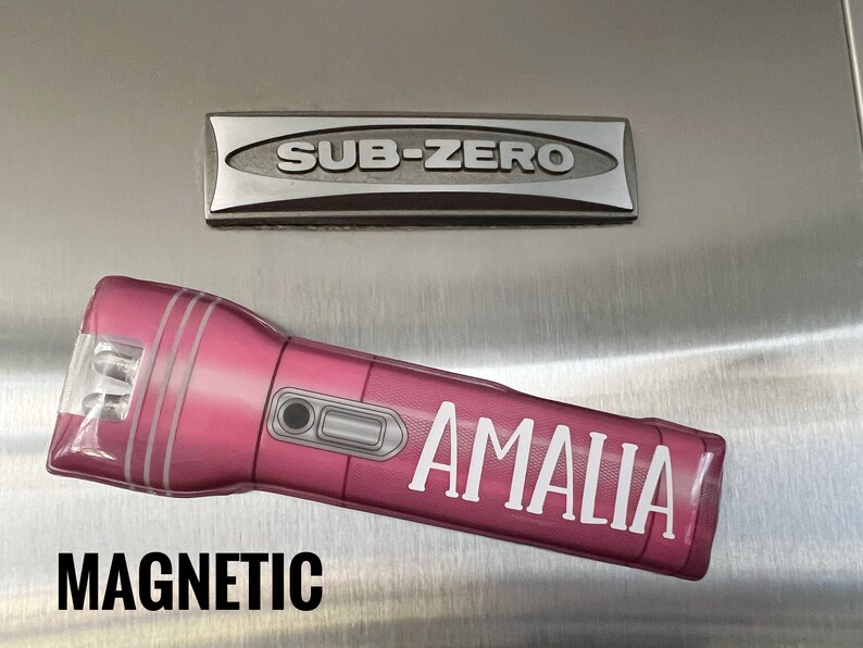 Peut inclure: Une lampe de poche magn&eacute;tique rose avec le nom "AMALIA" en lettres blanches. Le mot "MAGNETIC" est imprim&eacute; en lettres noires en gras sous la lampe de poche. Un embl&egrave;me argent&eacute; "SUB-ZERO" est au-dessus.