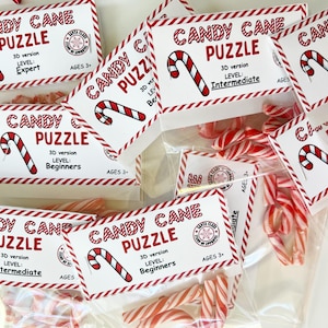 Puede incluir: Varias bolsas de pl&aacute;stico transparente llenas de bastones de caramelo rojos y blancos y piezas de rompecabezas. Cada bolsa tiene una etiqueta que dice "Candy Cane Puzzle" con un nivel de dificultad y un rango de edad.