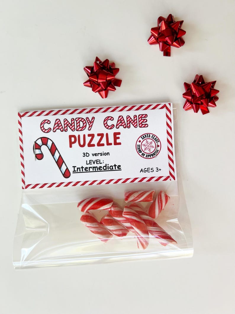 Puede incluir: Una bolsa transparente con bastones de caramelo rojos y blancos, con una etiqueta que dice "CANDY CANE PUZZLE" y el nivel "Intermedio". Tres lazos decorativos rojos est&aacute;n colocados alrededor de la bolsa. El rompecabezas es para mayores de 3 a&ntilde;os.
