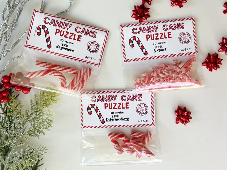 Puede incluir: Tres bolsas transparentes con rompecabezas de bastones de caramelo, cada una etiquetada como "Candy Cane Puzzle" con niveles de dificultad: Principiante, Experto e Intermedio. Los rompecabezas son para mayores de 3 a&ntilde;os.