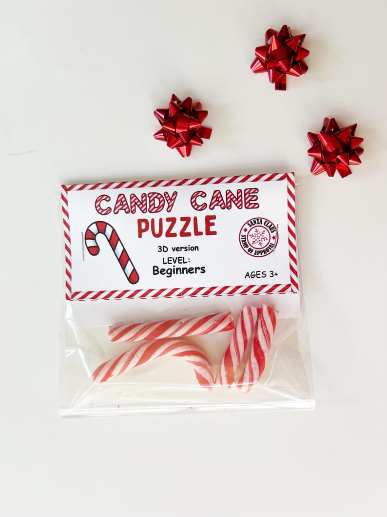 Puede incluir: Una bolsa transparente con bastones de caramelo a rayas rojas y blancas y un paquete de "Candy Cane Puzzle". El paquete tiene un borde rojo y blanco y presenta una ilustraci&oacute;n de bast&oacute;n de caramelo y el texto "3D version, Level: Beginners, Ages 3+". Tres lazos rojos est&aacute;n dispersos.
