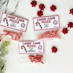 Puede incluir: Tres bolsas transparentes con rompecabezas de bastones de caramelo, cada una con una etiqueta que dice "Candy Cane Puzzle" y niveles de dificultad: Principiante, Experto e Intermedio. Las bolsas contienen bastones de caramelo a rayas rojas y blancas y caramelos triturados. Hay lazos rojos esparcidos.