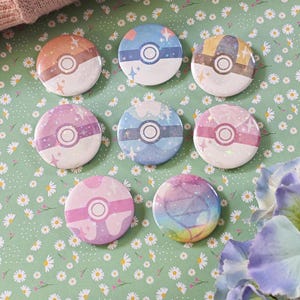Puede incluir: Conjunto de ocho pines redondos de colores con fondo blanco y una imagen estilizada de una Poké Ball con efecto brillante. Los pines están dispuestos en círculo sobre un fondo verde con flores blancas.