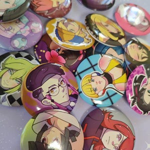 Peut inclure: Une collection de boutons ovales colorés avec des illustrations de personnages de style anime. Les boutons présentent divers personnages avec des coiffures et des expressions variées, sur des fonds vibrants. Les boutons sont dispersés sur une surface violet clair.