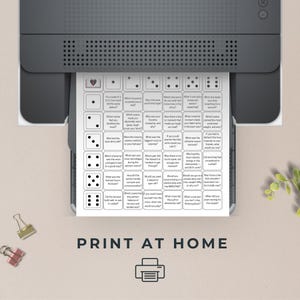 Op de afbeelding: Een witte afdruk met een dobbelspelontwerp komt uit een printer. De afdruk heeft een raster met vragen en dobbelsteenpictogrammen. De tekst "PRINT AT HOME" staat onderaan, met een printerpictogram.