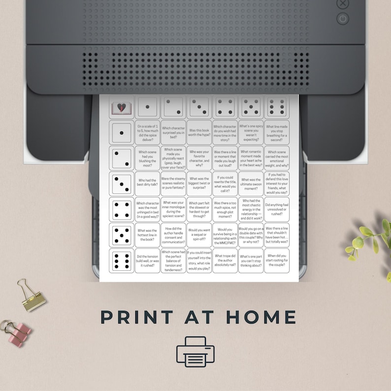 Op de afbeelding: Een witte afdruk met een dobbelspelontwerp komt uit een printer. De afdruk heeft een raster met vragen en dobbelsteenpictogrammen. De tekst "PRINT AT HOME" staat onderaan, met een printerpictogram.