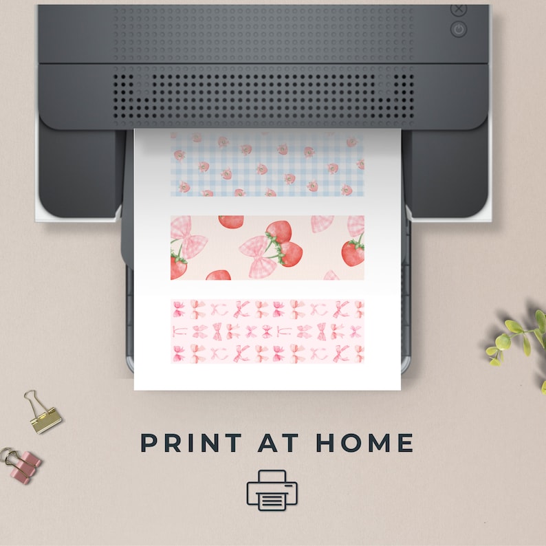 May include: A dark gray printer outputting a white sheet of paper featuring three horizontal strips with patterns. The top strip has blue gingham with strawberries, the middle has strawberries and pink bows, and the bottom has pink bows. Text reads PRINT AT HOME.