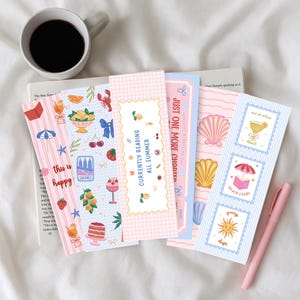 May include: A collection of five rectangular paper bookmarks featuring colorful summer-themed illustrations including seashells, fruit, drinks, and text that reads "currently reading all summer", "just one more chapter", "out of office", "beach reads", and "sunny days".
