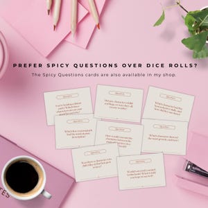 Op de afbeelding: Spicy Questions kaarten met vragen op een roze achtergrond. Een kopje koffie, potloden en een plant zijn ook aanwezig. De kaarten bevatten vragen over boeken en personages. Tekst: PREFER SPICY QUESTIONS OVER DICE ROLLS?