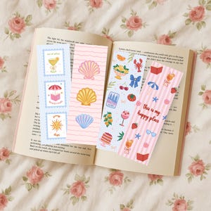 May include: Four rectangular paper bookmarks featuring colorful illustrations. One has blue stripes and icons of a drink, a book under an umbrella, and a sun. Another has pink waves and three seashells. Two others feature patterns of fruit, food, and summer items.