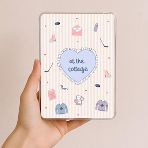 May include: Clear tablet case featuring a cream-coloured striped background with various illustrations. The design includes a blue heart with the text "at the cottage", hockey sticks, ice skates, and sweaters. Other illustrations include a duck, a book, and an envelope.