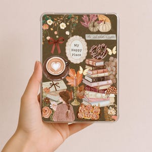 Puede incluir: Una funda de tableta rectangular transparente con fondo marrón oscuro e ilustraciones otoñales que incluyen una taza de café con arte latte de corazón, libros apilados, rollos de canela, una persona con suéter, calabazas y el texto My Happy Place.