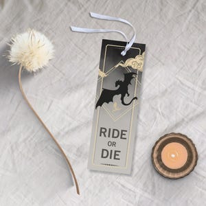 May include: A black and gold bookmark with a silhouette of a dragon and the text "Ride or Die".