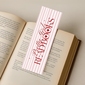 May include: A pink and white striped bookmark with the text "Pretty Girls READ BOOKS" in red script. The bookmark is inserted into an open book with aged pages, creating a literary theme.