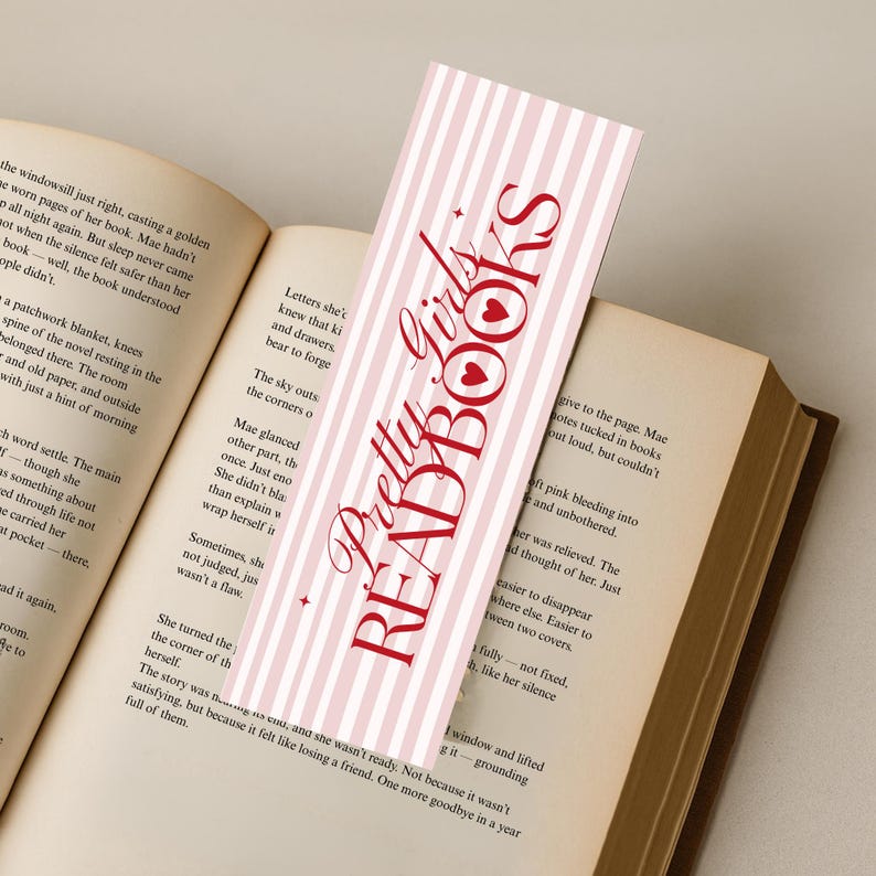 May include: A pink and white striped bookmark with the text "Pretty Girls READ BOOKS" in red script. The bookmark is inserted into an open book with aged pages, creating a literary theme.