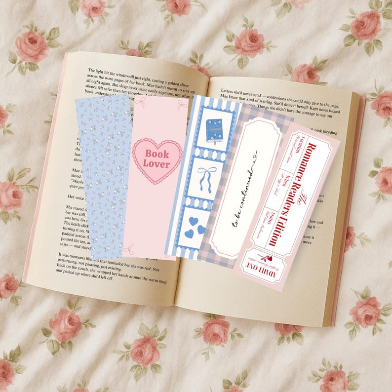 May include: An open book with several decorative bookmarks. The bookmarks feature floral patterns, hearts, and text like "Book Lover" and "Romance Readers Edition." The color palette includes pink, blue, and white.