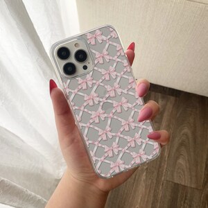 May include: A clear phone case with a pink and white bow pattern. The case is designed for an iPhone.