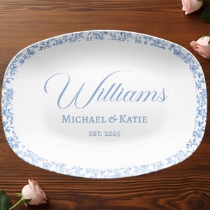 Puede incluir: Plato ovalado blanco con un borde floral azul. El plato tiene el nombre "Williams", los nombres "Michael & Katie" y el año "EST. 2025" en escritura azul claro.