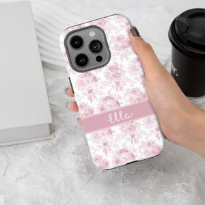 Op de afbeelding: Een witte telefoonhoes met een roze bloemenpatroon en de naam "Ella" gedrukt op een roze band.
