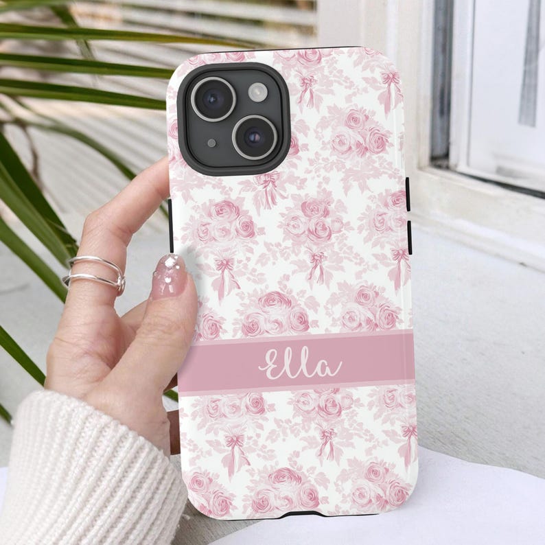 Op de afbeelding: Een roze en witte bloemen telefoonhoesje met een roze streep en de naam "Ella" in wit.