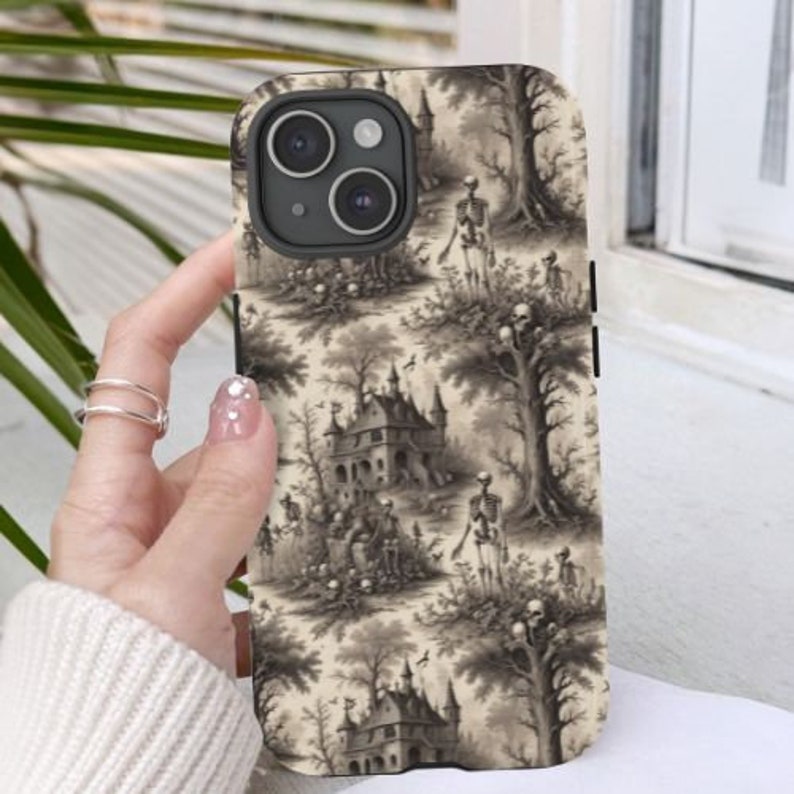 Puede incluir: Una funda para tel&eacute;fono en blanco y negro con un dise&ntilde;o espeluznante de inspiraci&oacute;n vintage que presenta esqueletos, una casa encantada y &aacute;rboles. La funda tiene un recorte para el objetivo de la c&aacute;mara.