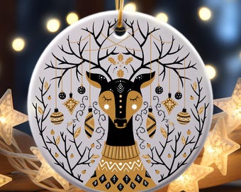 May include: A white ceramic Christmas ornament with a black and gold deer design. The deer has a gold sweater and closed eyes. The ornament is decorated with gold and black ornaments and branches.