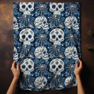 May include: A blue fabric kitchen towel with a repeating pattern of white sugar skulls with floral details and spiderwebs.