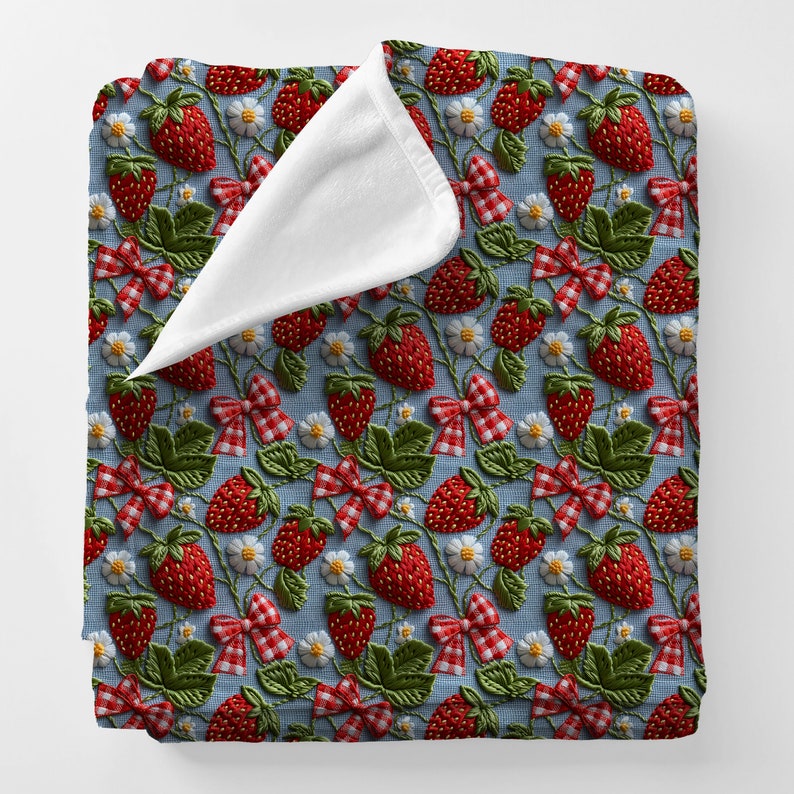 May include: A blue and white throw blanket with a repeating pattern of embroidered red strawberries, green leaves, and white flowers. The blanket has a white fleece backing.