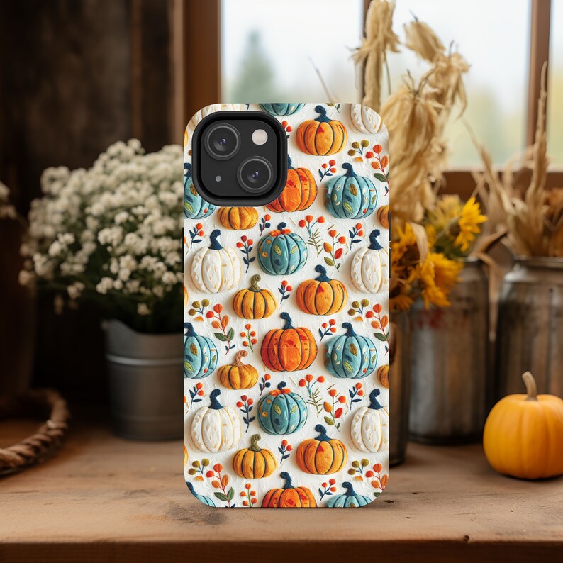 Peut inclure: Une coque de t&eacute;l&eacute;phone blanche avec un motif de citrouilles orange, blanches et bleues. La coque a un d&eacute;coupage pour l'objectif de l'appareil photo noir.