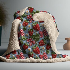 May include: A soft, plush throw blanket with a blue and white checkered background featuring a repeating pattern of embroidered red strawberries and white bows.